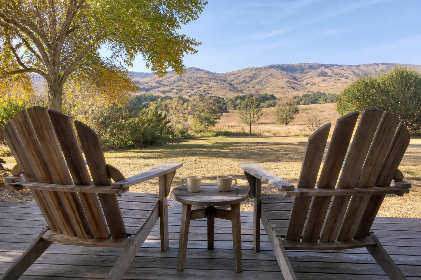Two coffee mugs on a small table between two chairs on a wooden deck